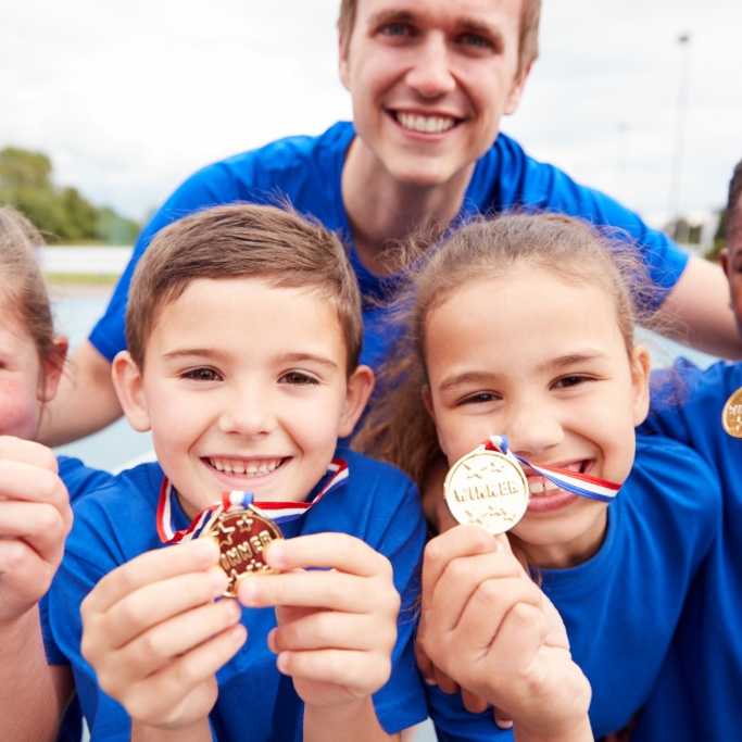 Portrait Of Children With Male Coach Showing Off Winners Medals On Sports Day